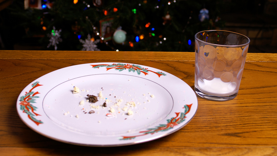 Leerer Teller mit Kekskrümeln und leerem Glas Milch am Weihnachtsbaum