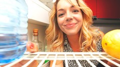 Junge Frau schaut lächelnd in leeren Kühlschrank
