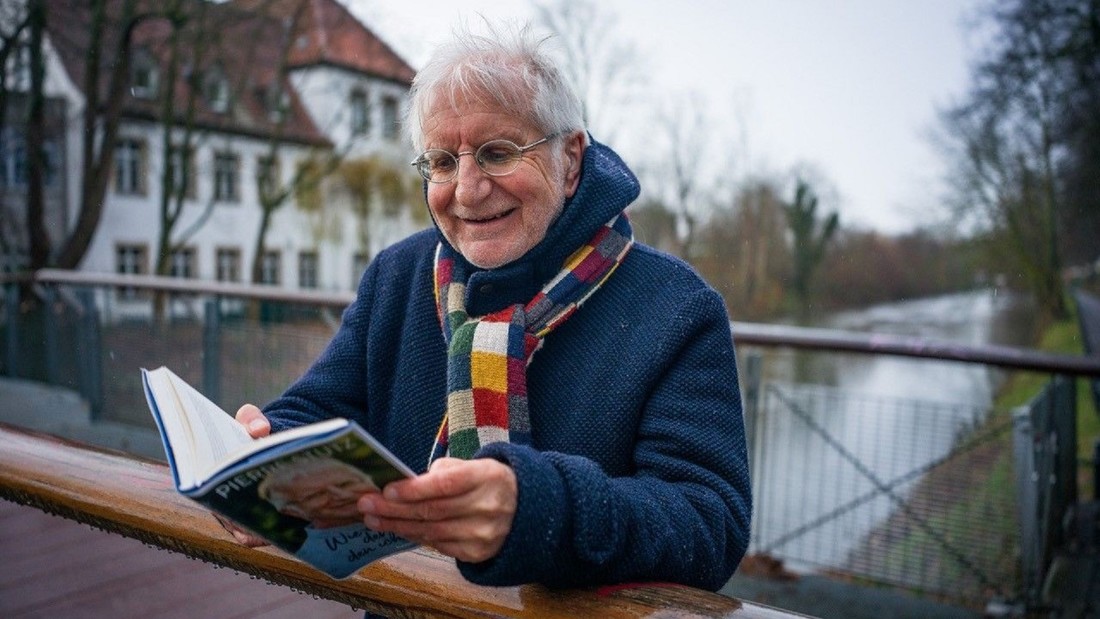 Der Ex-Priester und Buchautor Pierre Stutz steht mit einem aufgeschlagenen Buch auf einer Brücke 