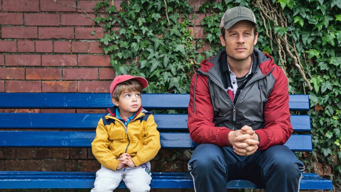 Der vierjährige Sohn schaut seinen Vater an. Beide sitzen auf einer Holzbank im Freien
