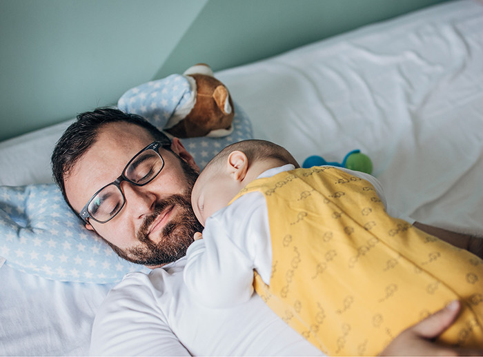 Junger Vater mit seinem Baby schlafend im Bett 