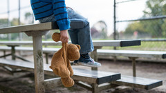 Junge mit teddy sitzt  einsam auf Tribüne