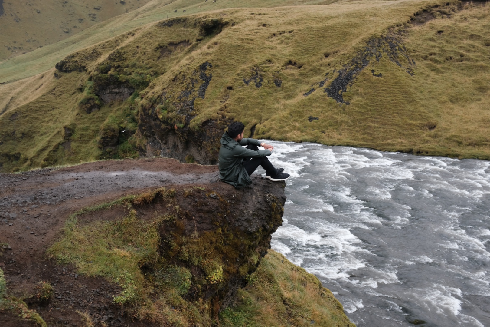 Mann sitz an Klippe vor Wasserfall