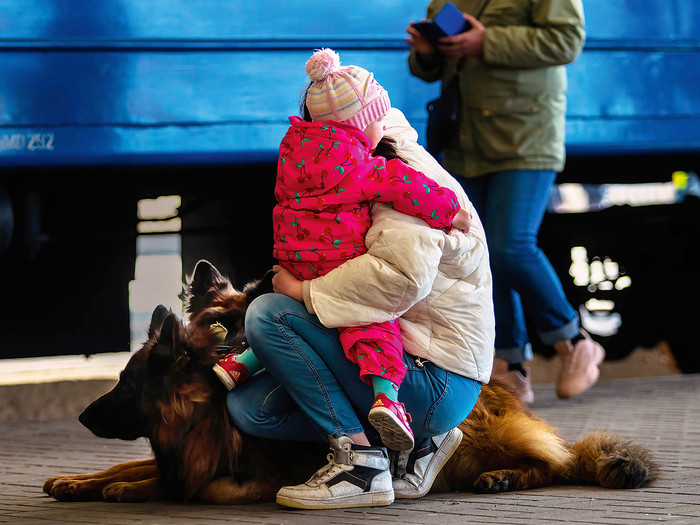Mutter mit Kind und zwei großen Hunden kniet auf einem Bahnsteig. Der Zug hinter ihnen hat Geflüchtete aus Mariupol 