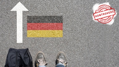 Mann mit Tasche steht vor Deutschlandflagge am Boden