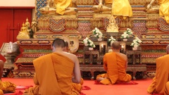 Buddhistische Mönche aus Thailand in orangefarbenen Gewändern sitzen im Schneidersitz auf dem Boden.