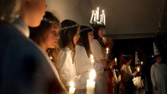 Mädchen mit langen Haaren, weißen Gewändern und Kerzen in den Händen stehen in einer Reihe nebeneinander