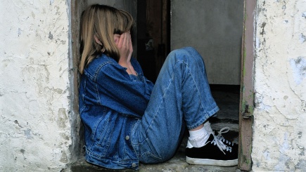 Ein Mädchen in Jeans sind zusammengekauert in einer Maueröffnung mit den Händen vorm Gesicht