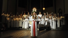 Ein Mädchen trägt einen Kranz mit brennenden weißen Kerzen auf dem Kopf, sie ist umgeben von weiteren Mädchen.
