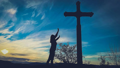 Frau betet draußen in der Natur zu großem Kreuz