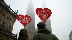 Ein Paar demonstriert mit Herzschildern mit der Aufschrift "Demokratie" auf dem Marktplatz in Bremen gegen die gemeinsame Abstimmung von Union und AfD für eine schärfere Migrationspolitik.