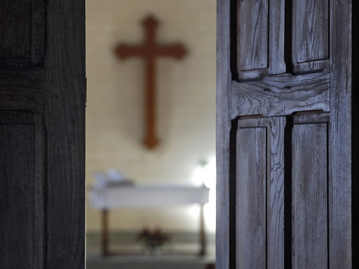 Geöffnete Kirchetür mit Blick auf den Altar mit einem Kreuz