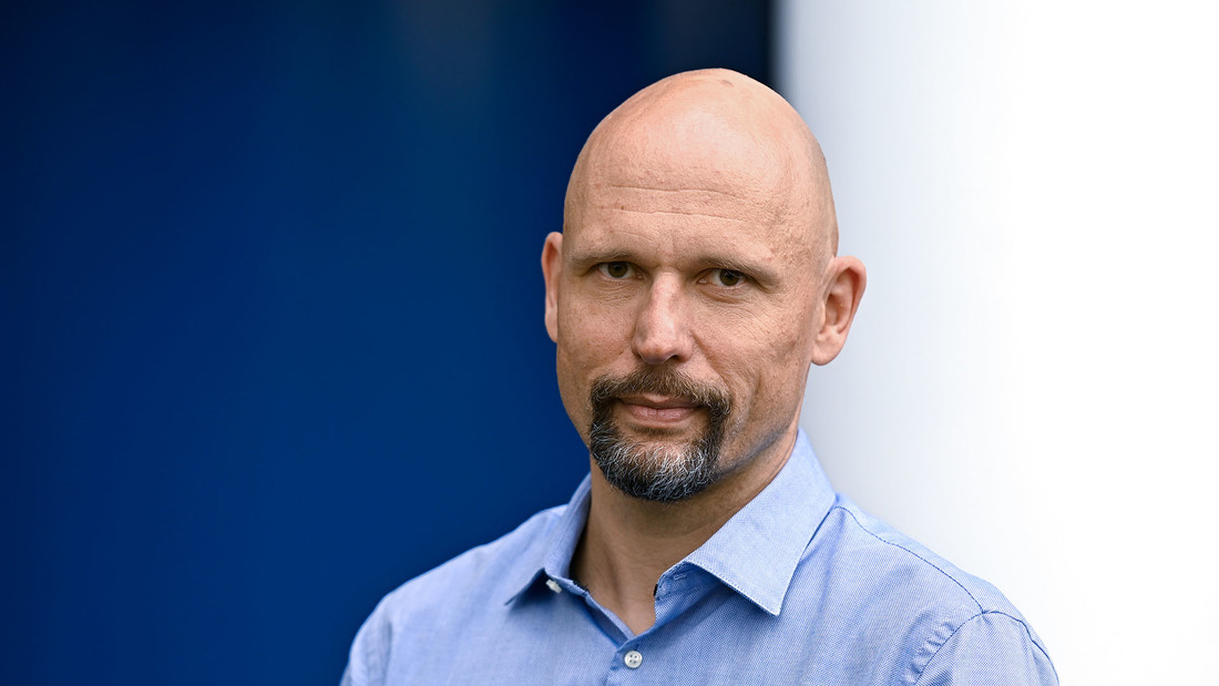 Portrait vom epd-Chefredakteur Karsten Frerichs vor blau-weißer Wand.