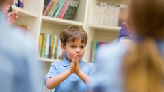 Junger Schüler hält die Hände in einem Klassenraum zum Gebet vor sich.
