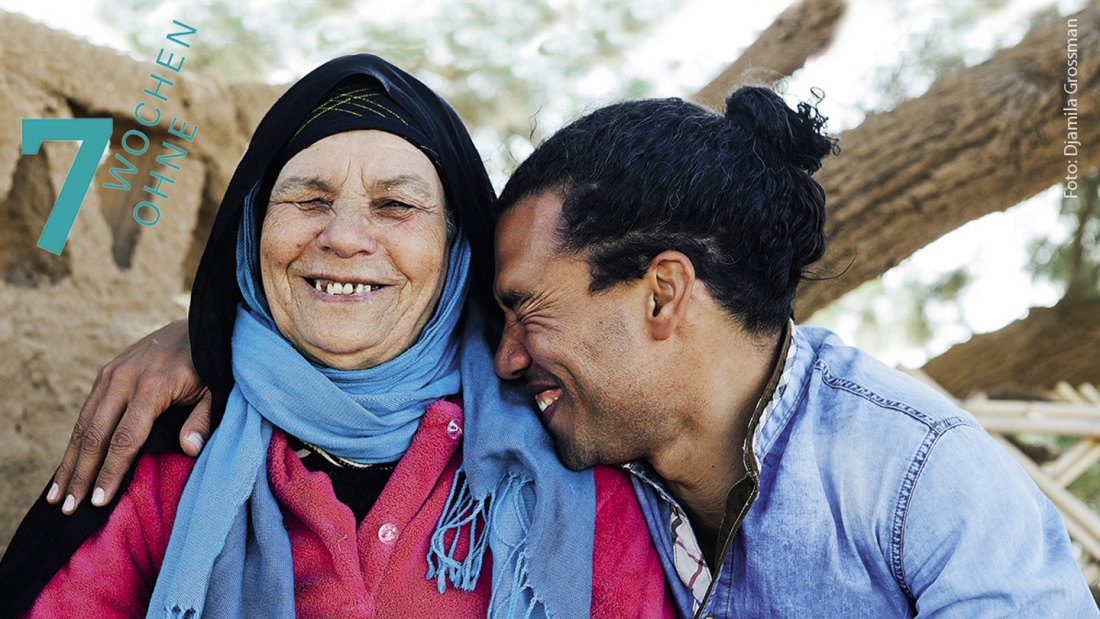 Ein mann lehnt sich an seine Kopftuchtragende Mutter und lacht.