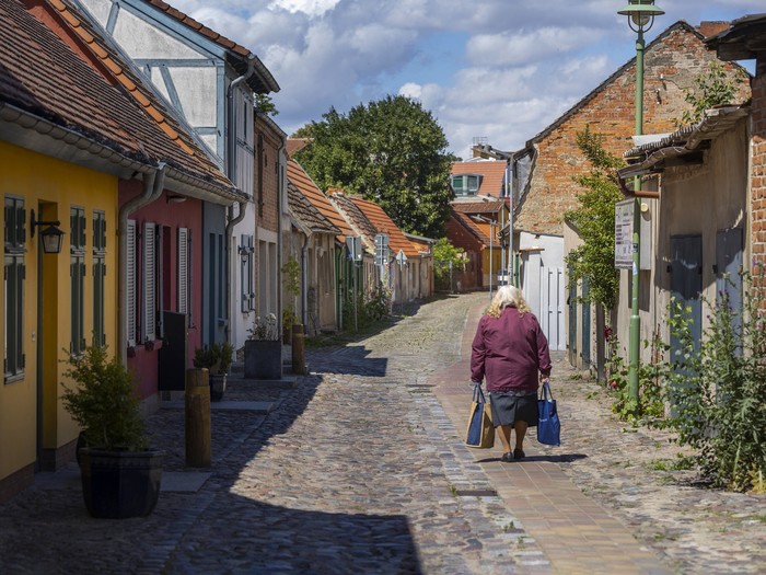 Eine ältere Frau läuft mit Einkaufstaschen in der Kleinstadt Altentreptow in Mecklenburg Vorpommern eine leere Gasse entlang