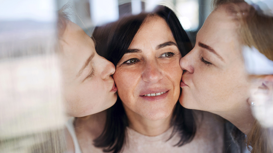 Zwei Töchter küssen ihre Mutter auf die Wange