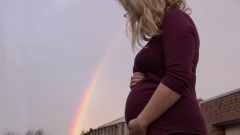 Schwangere Frau mit Regenbogen im Hintergrund.