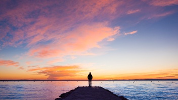 Mann steht am Meer vor Sonnenuntergang