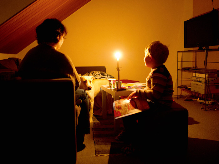 Eine Mutter sitzt mit ihrem Sohn in ihrer abgedunkelten Wohnung . Nur eine brennende Kerze erleuchtet den Raum.  Nach vielen offenen Rechnungen und Schulden hatten die Stadtwerke den Strom abgeschaltet