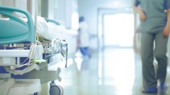 Krankenhausflur mit Personal im Hintergrund und Krankenbett auf Rollen im Vordergrund