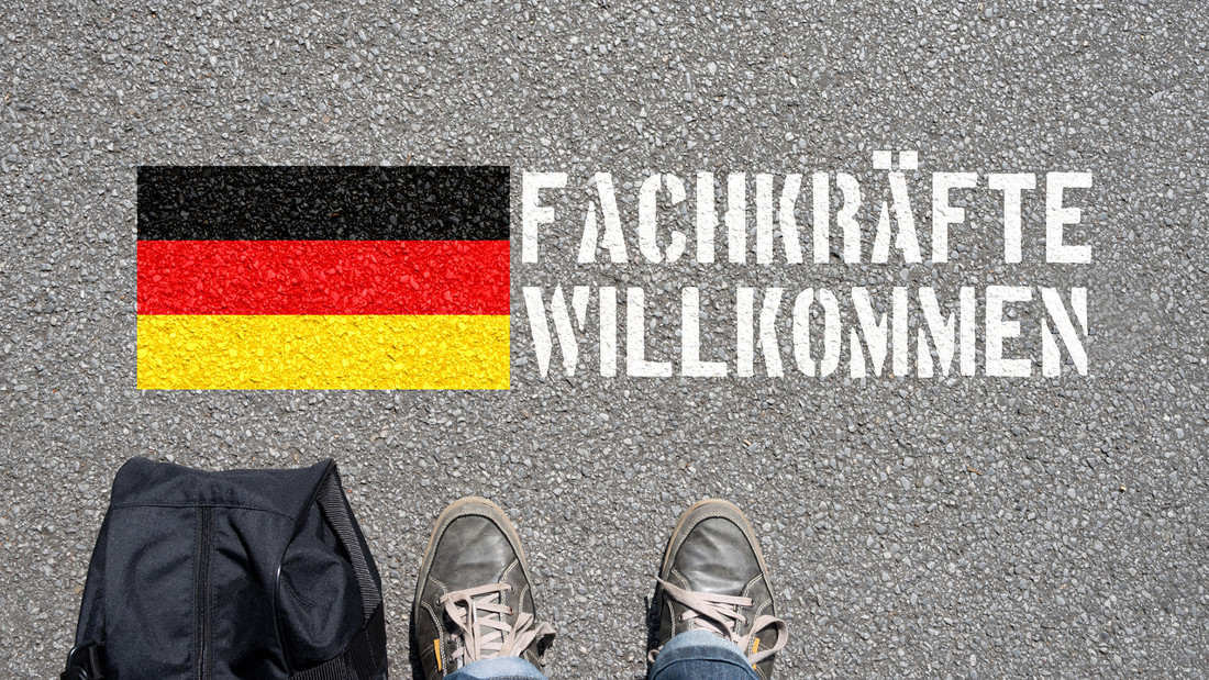 "Fachkräfte willkommen" steht neben Deutschlandflagge auf Straße