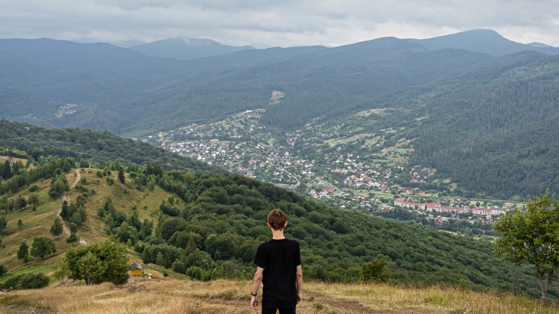 Person schaut von einem Hügel auf ein Dort im Tal