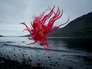 Perücke mit roten Haaren schwebt durch mystische Küstenlandschaft in Norwegen