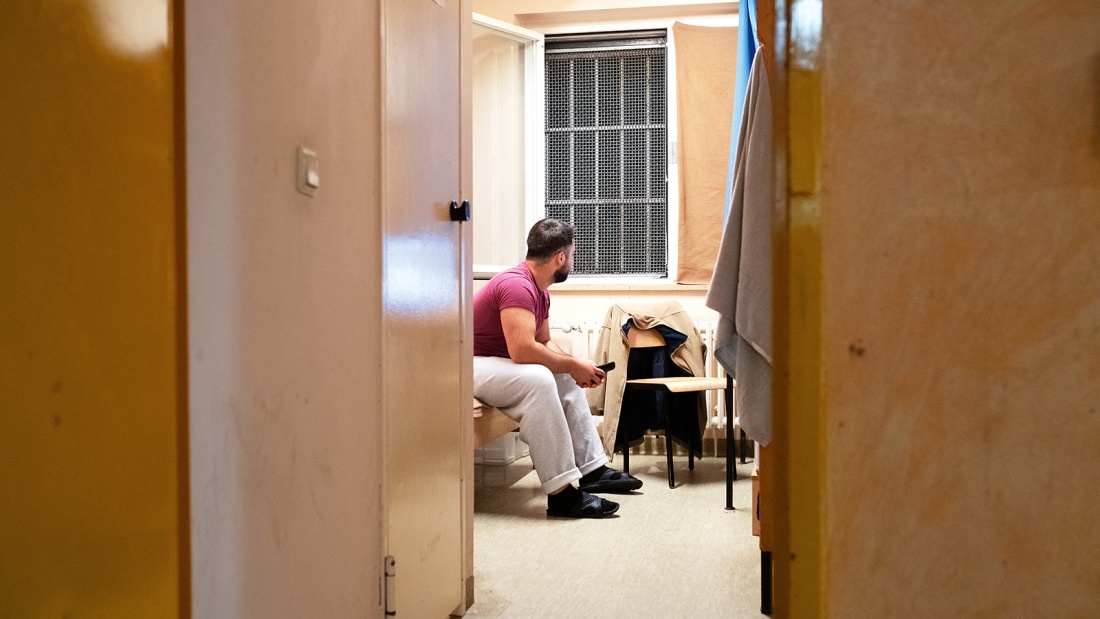 Ein Häftling mit abgewandtem Blick sitzt in der Zelle auf seiner Pritsche