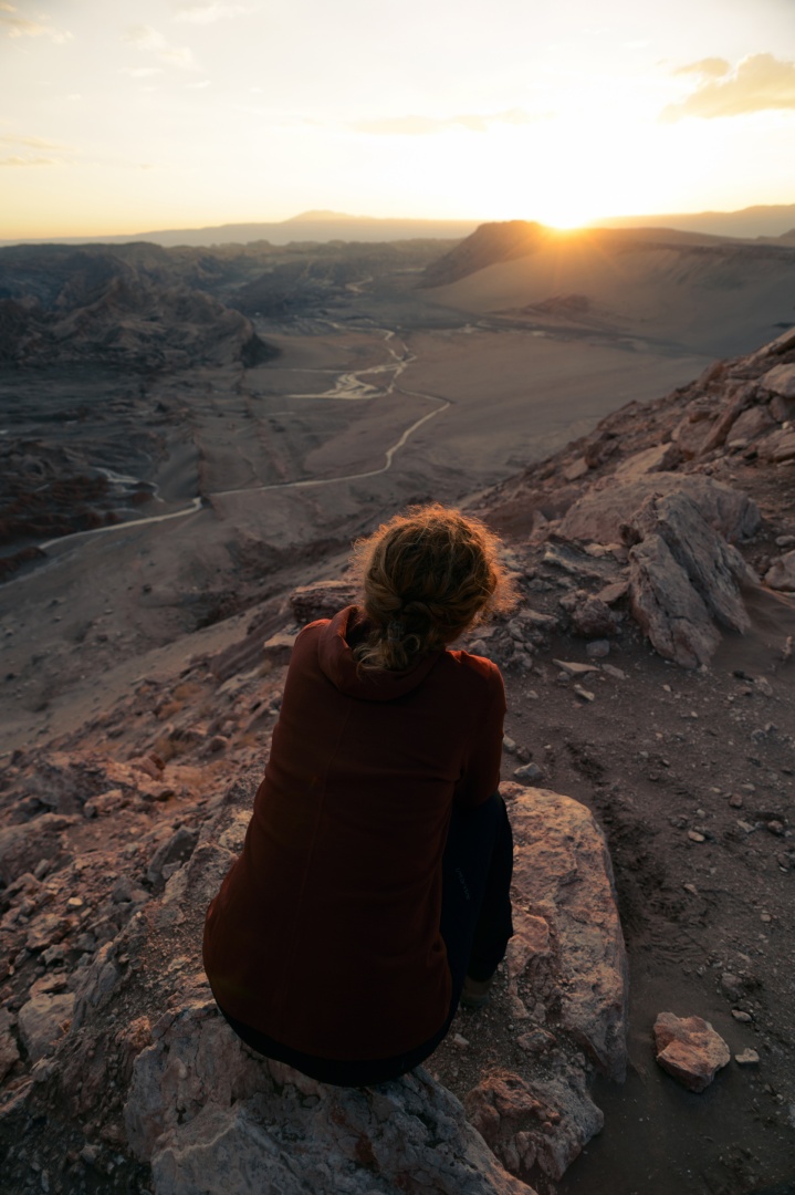 Eine Frau sitzt auf einem Felsen und beobachtet den Sonnenaufgang.