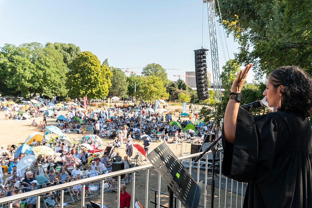 Sarah Vecera von der Vereinten Evangelischen Mission predigt von einer vier Meter hohen Empore aus über die biblische Speisung der 5000