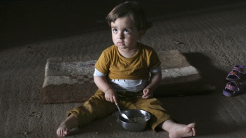 Jesidisches Kind sitzt auf dem Boden und isst