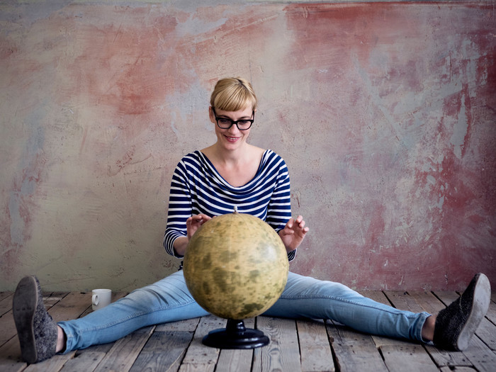 Junge Frau sitzt am Boden vor einem Globus