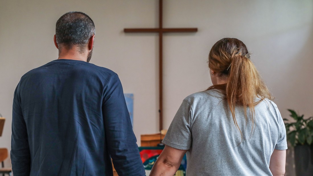 Ein kurdisch-irakisches Paar steht mit dem Rücken zum Betrachter vor dem Altarkreuz in einer Kirche 