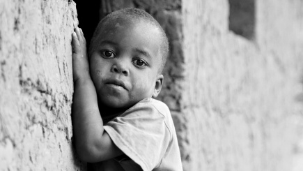 Ein einsames afrikanisches Kind lehnt an einer Hausmauer