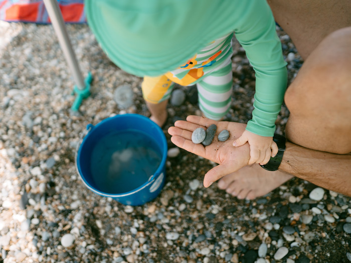 Kind mit Vater am Strand, mit Steinen in der Hand