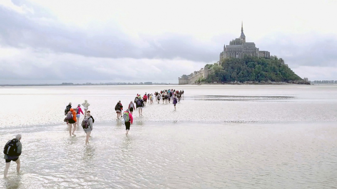 Eine Gruppe Menschen läuft auf den Mont St. Michel zu.