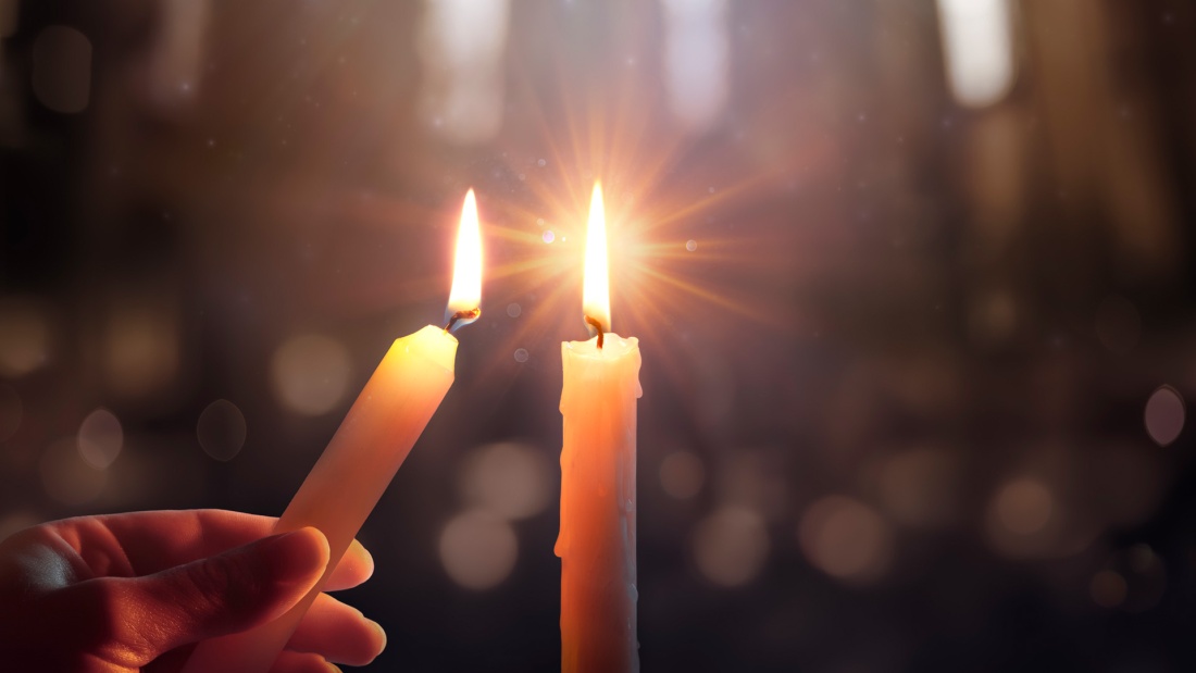 Kerze wird angezündet  an einer anderen Kerze in der Kirche