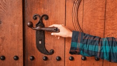 Frau legt Hand auf Türklinke einer Kirchentür