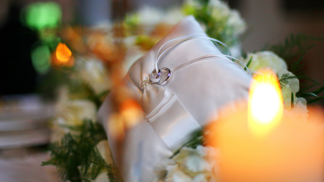 Eheringe liegen in einer Kirche auf einem weißen Kissen mit Kerzen und Blumen umgeben.