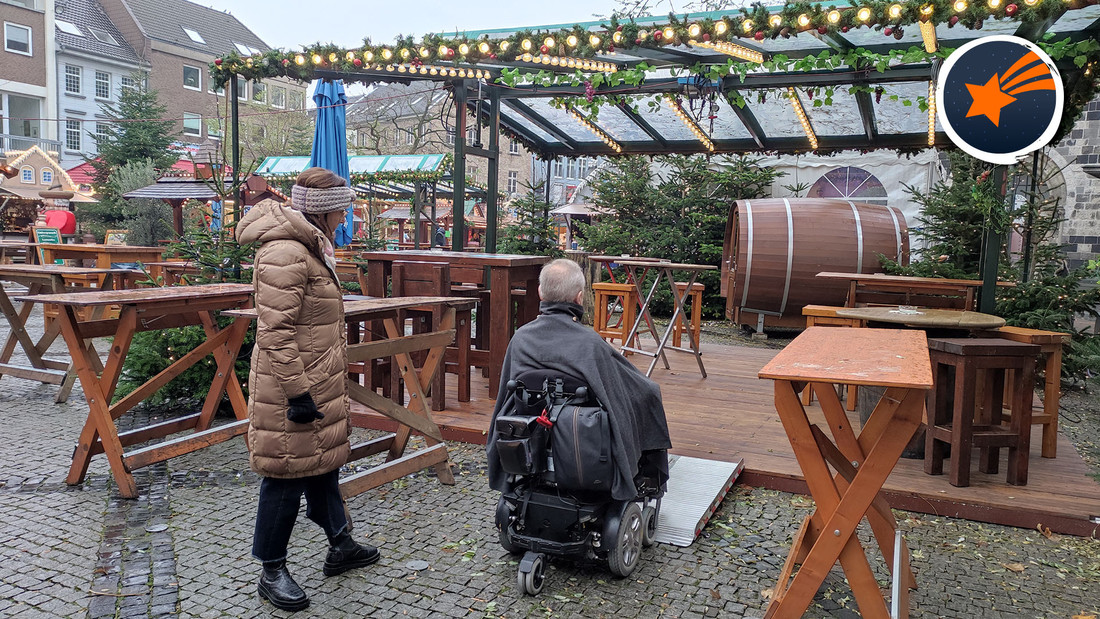 Rollstuhlfahrer und zwei Besucher stehen auf dem Weihnachtsmarkt