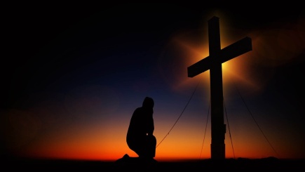 Ein Mann kniet vor einem Kreuz in der Abenddämmerung