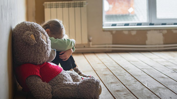 Trauriges Kind mit Teddy in vernachlässigter Wohnung