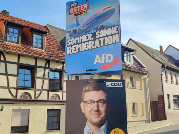 Wahlplakate zur Landtagswahl: AfD-Wahlplakat mit der Aufschrift "Der Osten machst - Sommer, Sonne, Remigration"; auf dem Flugzeug steht in kleiner Schrift "Abschiebe-Hansa"; darunter CDU-Plakat mit Christoph Zippel