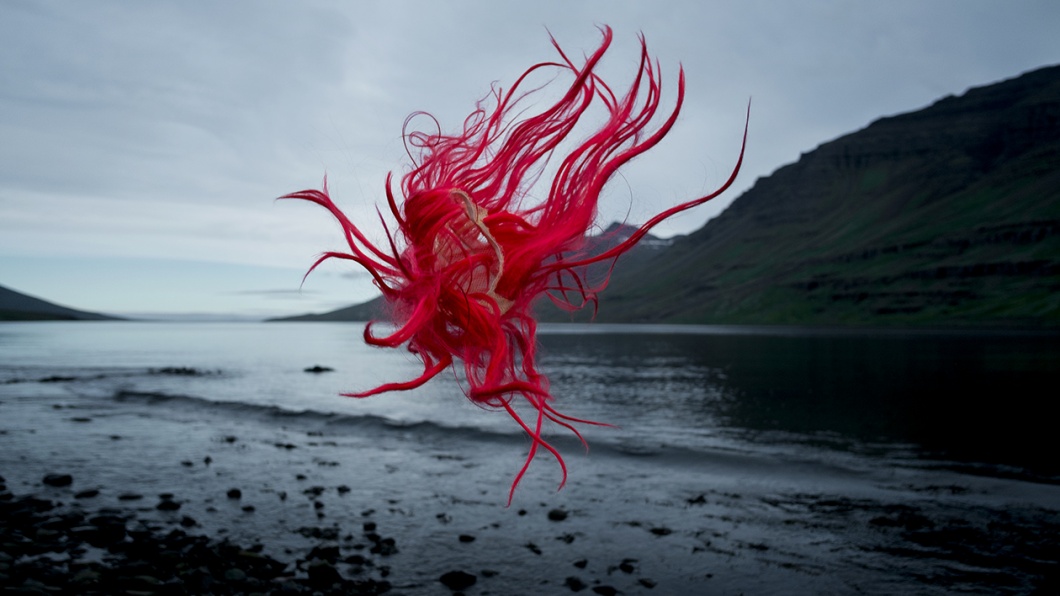 Perücke mit roten Haaren schwebt durch mystische Küstenlandschaft in Norwegen