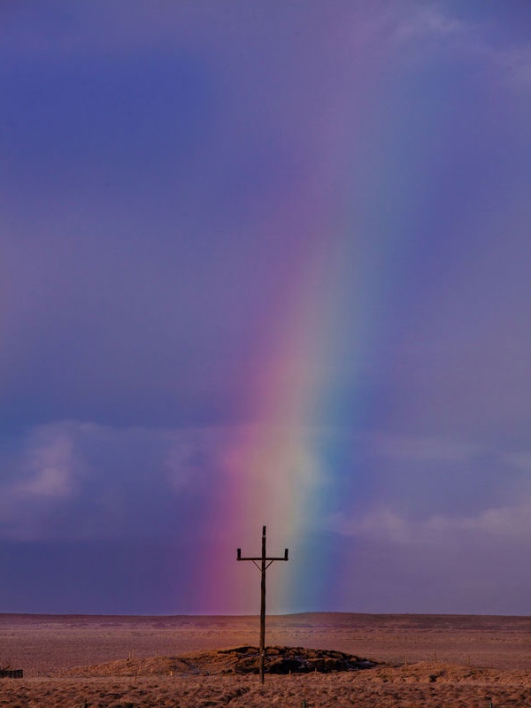 Strommast in der Wüste mit Regenbogen dahinter