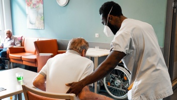 Eine Pflegekraft hilft einem Mann aus dem Rollstuhl