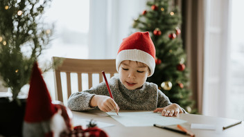 Junge mit Weihnachtsmannmütze schreibt Wunschzettel