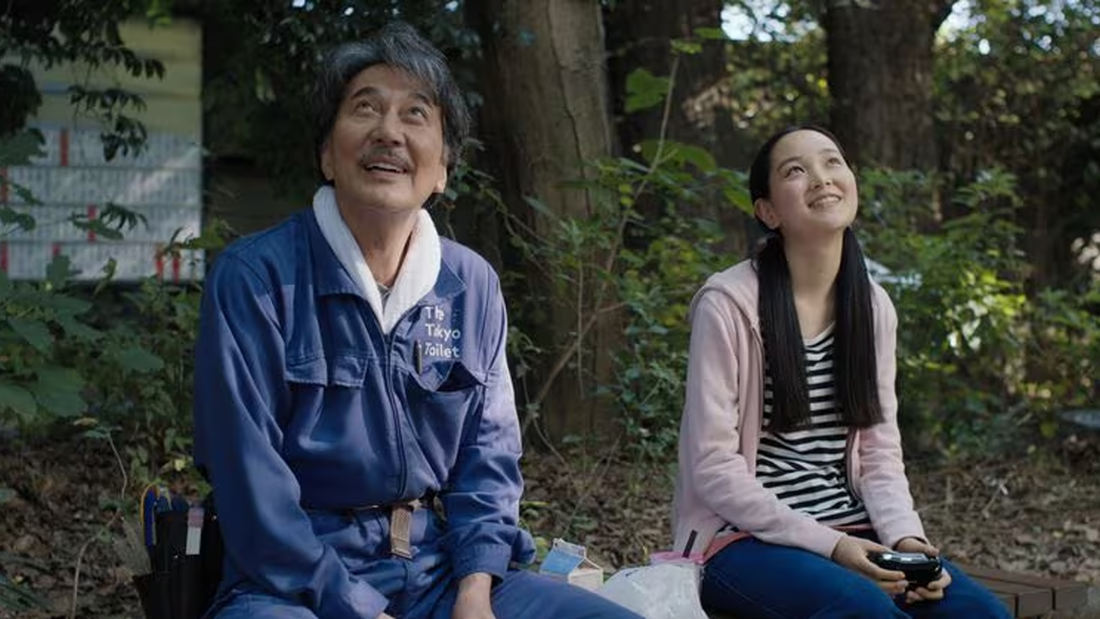 Ein japanischer Mann und eine japanische Frau sitzen auf einer Parkbank und schauen zu einer Drohne im Himmel, die sie steuern