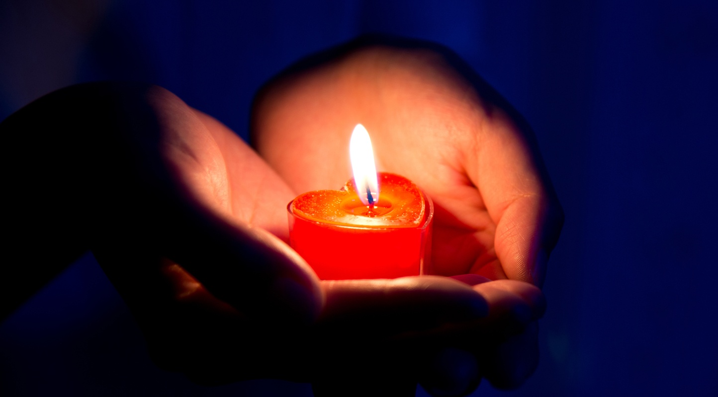 Eine rote, herzförmige Kerze wird in der Hand gehalten.